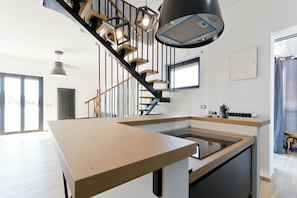 A modern kitchen with a central island, a staircase with wooden steps and black railings, pendant lighting, and a large window. - Pescara Beach Tramonto (Pescara)