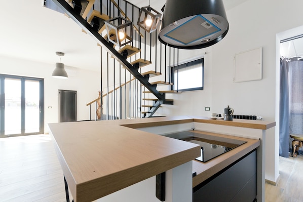 A modern kitchen with a central island, a staircase with wooden steps and black railings, pendant lighting, and a large window. - Pescara Beach Tramonto (Pescara)