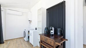 Uma cozinha compacta com máquina de lavar, cafeteira e radiador.