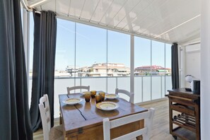 Un espace repas comprenant une table, des chaises et une vue sur les bâtiments, grâce à de grandes fenêtres.
