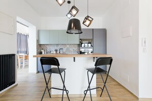 A modern kitchen with a central island, two black bar stools, and pendant lighting. - Pescara Beach Tramonto (Pescara)