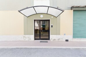A building entrance with a glass door, a small awning above, and a green shutter door to the right. - Pescara Beach Tramonto (Pescara)