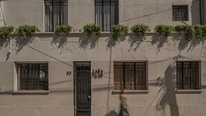 Eine Gebäudefassade mit mehreren Fenstern, von denen einige Fensterläden haben, und einer Tür mit einem Metallgitter.