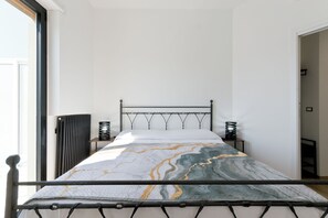 Una cama con estructura metálica, una colcha con estampado de mármol y dos mesitas de noche con jarrones decorativos.