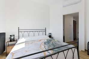 Ein modernes Schlafzimmer mit einem Metallbettgestell, einer Bettdecke mit Marmoroptik und einem Heizkörper links.