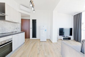 A modern kitchen with a built-in oven, a refrigerator, and a dining area with a sofa and a flat-screen TV. - Pescara Beach Alba - One Bedroom Apartment, Sleeps 4 (Pescara)
