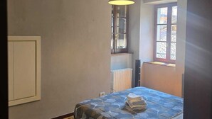 Un dormitorio con cama, lámpara colgante, ventana y radiador.