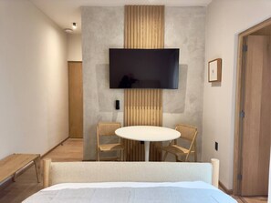 Ein Hotelzimmer mit einem Bett, einem runden Tisch mit Stühlen, einem Flachbildfernseher an der Wand und einer Holztür.