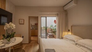 A hotel room with a bed, a small table with a plant, a kitchenette, and a sliding door to a balcony with plants. - Beautiful loft with private patio & A/C (Ciudad de México)
