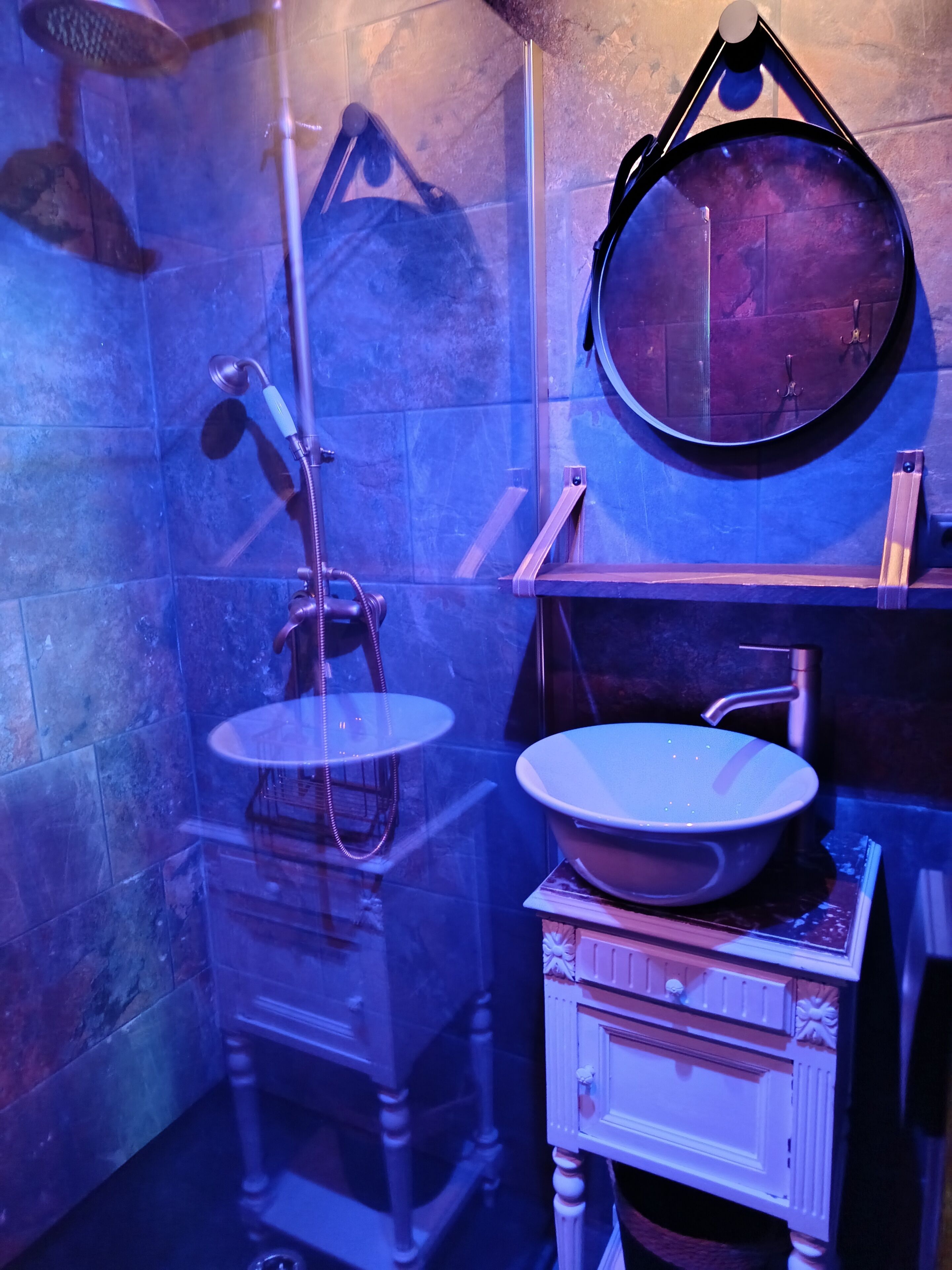 Een badkamer met een douchecabine van glas, een ronde spiegel en een witte wastafel.