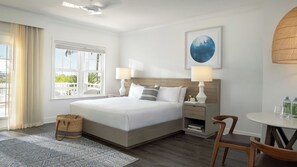 Ein Hotelzimmer mit einem großen Bett, zwei Nachttischen mit Lampen, einem kleinen runden Tisch mit Stühlen, einem Korbwäscheschrank und Blick auf Grünflächen.