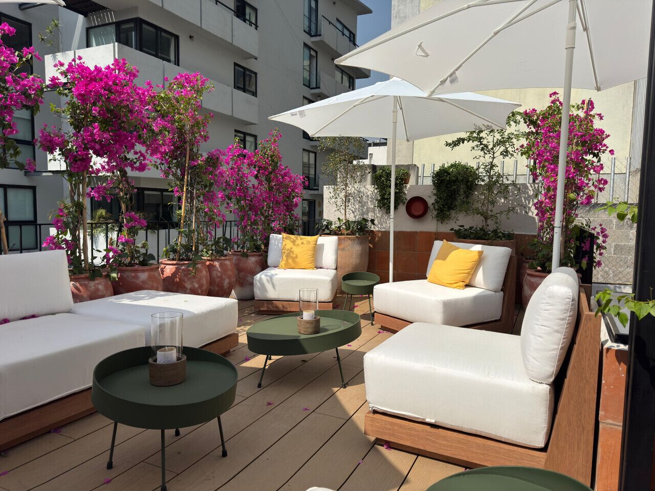 Ein Außenbereich mit weißen Sofas, runden grünen Tischen und großen weißen Sonnenschirmen.