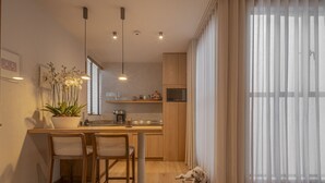 Una cocina moderna con armarios de madera, una zona de comedor con dos sillas, una orquídea en maceta y un perro acostado en el suelo.