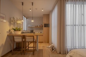 Eine moderne Küche mit Holzschränken, ein Essbereich mit zwei Stühlen, eine Topfpflanze mit Orchidee und ein Hund, der auf dem Boden liegt.