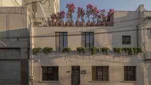 Un edificio con entrada a nivel de calle, ventanas en los pisos superiores y un balcón con plantas en macetas.
