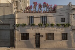 Ein Gebäude mit Eingang im Erdgeschoss, Fenstern in den oberen Stockwerken und einem Balkon mit Blumentöpfen.