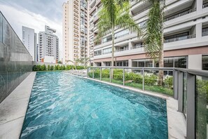 Una piscina con barrera de vidrio, rodeada de edificios altos y palmeras.