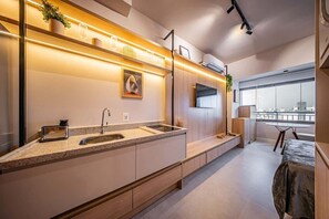 A modern kitchen with a built-in oven, a sink, and a countertop. There is a window with a view of the city. - GRAND VITRALLI (São Paulo)
