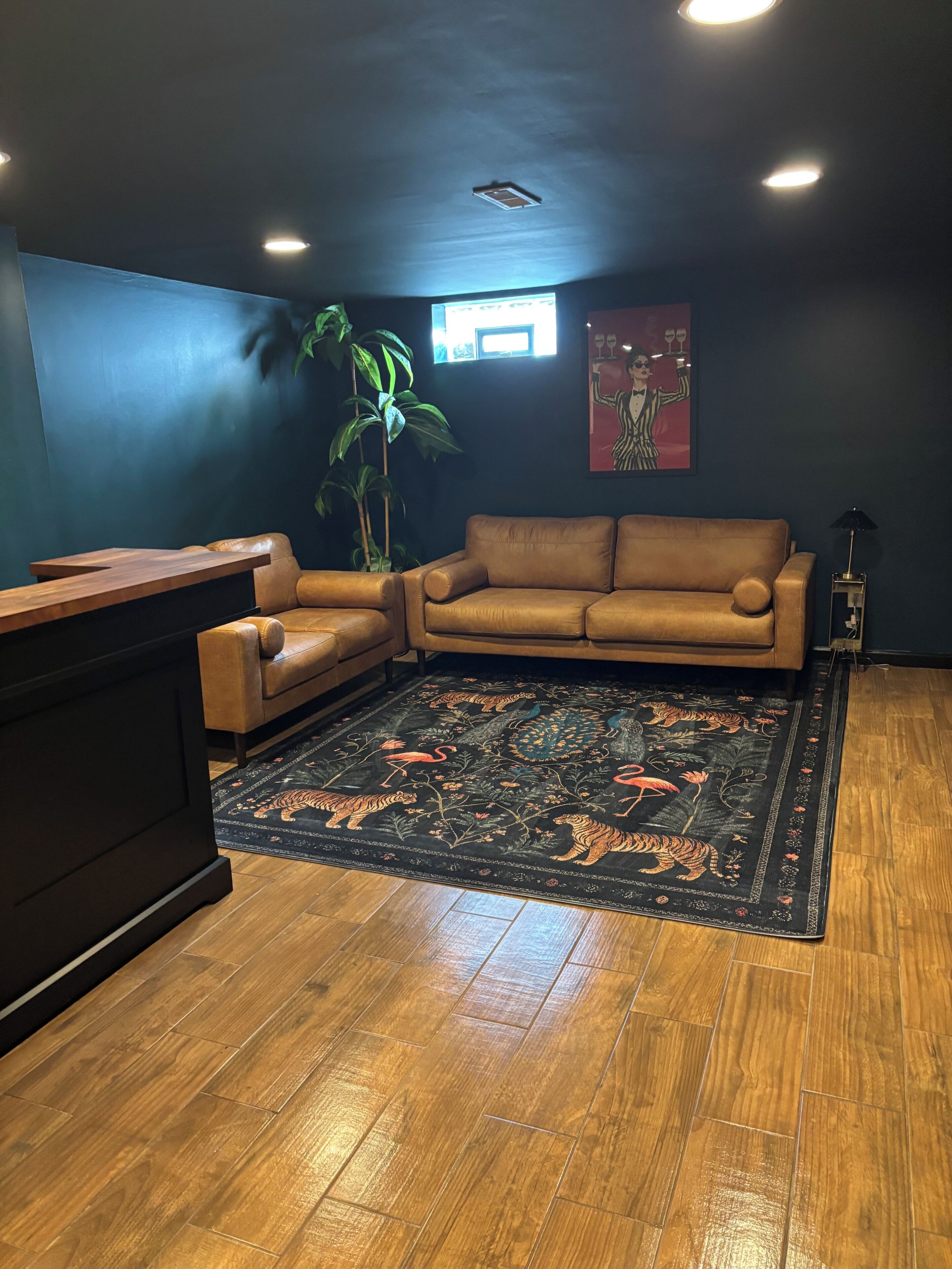 A room with a brown leather sofa, a wooden coffee table, a patterned rug, a potted plant, and a painting on the wall.