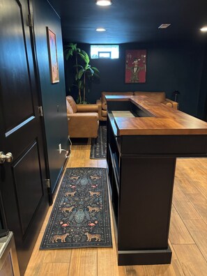 A modern kitchen with a wooden island, a dark-colored sofa, and a decorative rug. - The Birdhouse - Mid-Century Charm with a Speakeasy Lounge (Grove City)