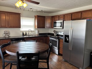 Una cocina con armarios de madera, un refrigerador de acero inoxidable, un microondas, una estufa y una mesa de comedor con sillas.