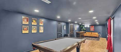 A pool table in a room with blue walls, wooden flooring, and framed pictures on the wall.