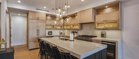 Una cocina moderna con una isla central, taburetes de bar, armarios de madera e iluminación colgante.
