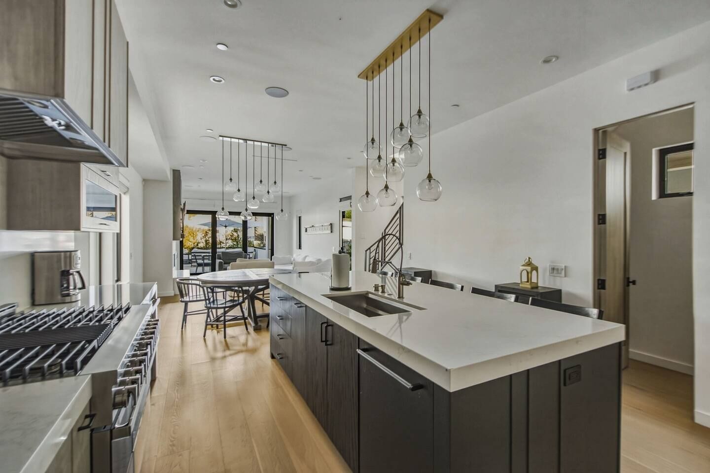 Une cuisine moderne dotée d’un grand îlot central, d’appareils électroménagers en acier inoxydable et de luminaires suspendus.