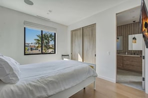 A bedroom with a bed, a window with a view, a door leading to a bathroom, and a small table. - Luxury Home On 7th - Patio, Deck, Fire Pit (Huntington Beach)