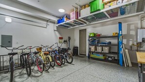 Un espace de rangement pour vélos, avec des vélos, des étagères contenant des boîtes de rangement et une porte donnant sur une autre pièce.