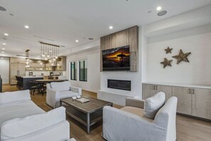 A modern living room with a fireplace, a dining area, and a kitchen in the background.