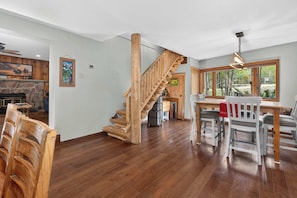 Uma sala de estar ampla com escada de madeira, mesa de jantar com cadeiras e lareira de pedra.
