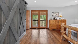 A bedroom with a wooden floor, a bed, a dresser, a lamp, and a sliding barn door. - Charming 3 Bed Cabin| Lakes, Hiking, Hot Tub (Grand Lake)