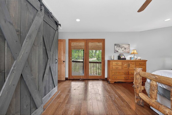 A bedroom with a wooden floor, a bed, a dresser, a lamp, and a sliding barn door. - Charming 3 Bed Cabin| Lakes, Hiking, Hot Tub (Grand Lake)