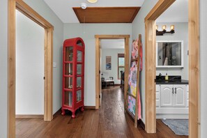A hallway with wooden flooring, a red telephone booth, a quilted wall hanging, and a kitchen area with white cabinets. - Charming 3 Bed Cabin| Lakes, Hiking, Hot Tub (Grand Lake)
