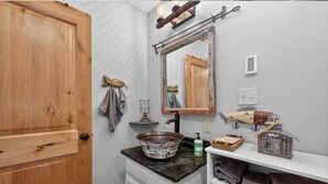 A bathroom with a wooden door, a mirror, a sink with a vessel basin, a towel rack, and a shelf with towels. - Charming 3 Bed Cabin| Lakes, Hiking, Hot Tub (Grand Lake)