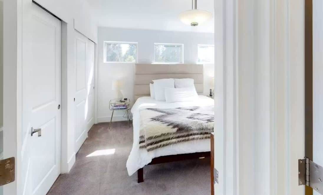 A bedroom with a bed, a bedside table, a lamp, and a window.