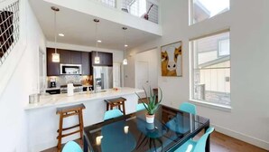 Una cocina moderna con una isla central, iluminación colgante y un comedor con una mesa de vidrio y sillas.