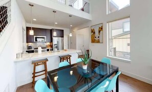 A modern kitchen with a central island, pendant lighting, and a dining area with a glass table and chairs. - Luxury Winter Park Condo| 2 Bed/ 2 Bath (Fraser)