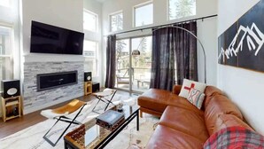 Una sala de estar moderna con chimenea, sofá de cuero y ventanas amplias.