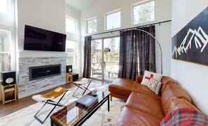 A modern living room with a fireplace, leather sofa, and large windows. - Luxury Winter Park Condo| 2 Bed/ 2 Bath (Fraser)