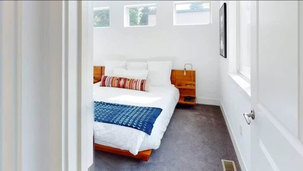 Un dormitorio con cama, mesita de noche, ventana y puerta.