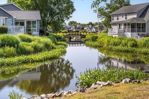 A residential area with a pond, houses with porches, and a wooden bridge. - Pond Front Home with Magnificent Sunset views from the gorgeous Screened porch! (Lewes)