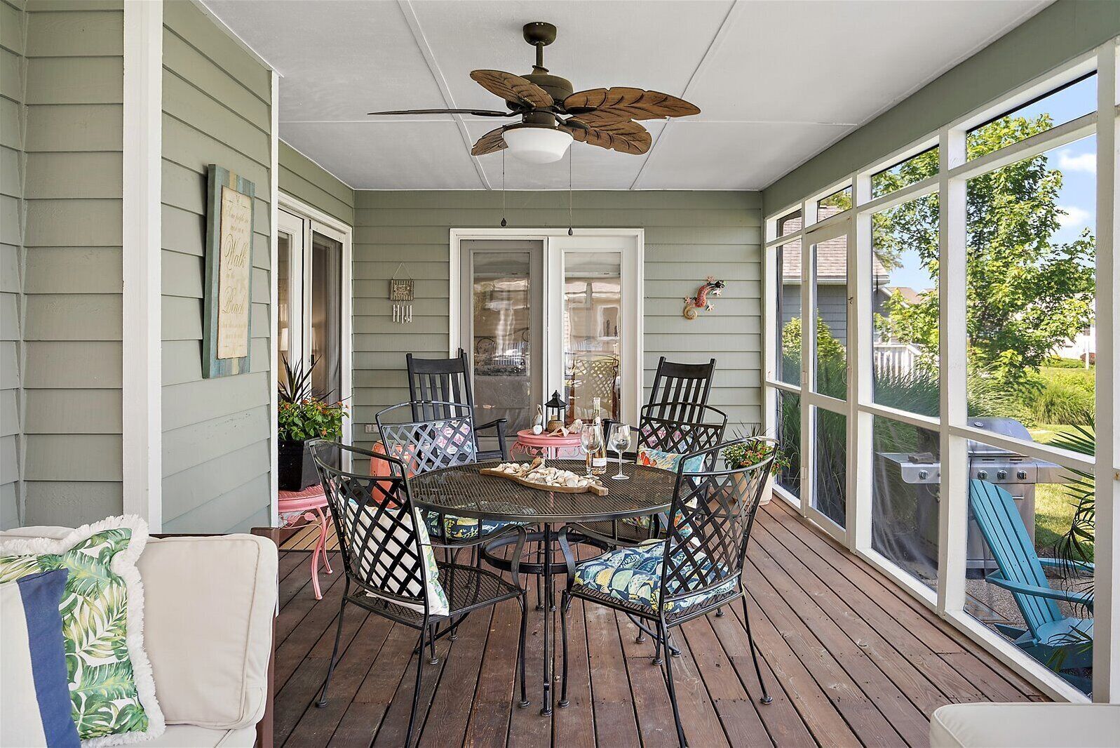 A covered outdoor dining area with a table and chairs, a ceiling fan, and a view of the outdoors.