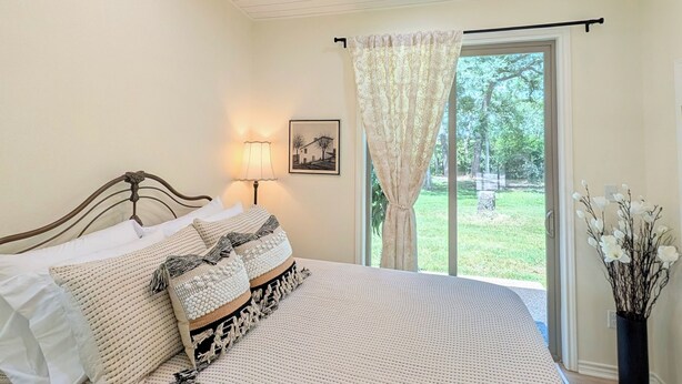 Une chambre à coucher avec un lit, un ventilateur de plafond, une fenêtre avec des rideaux et une table de chevet avec une lampe.