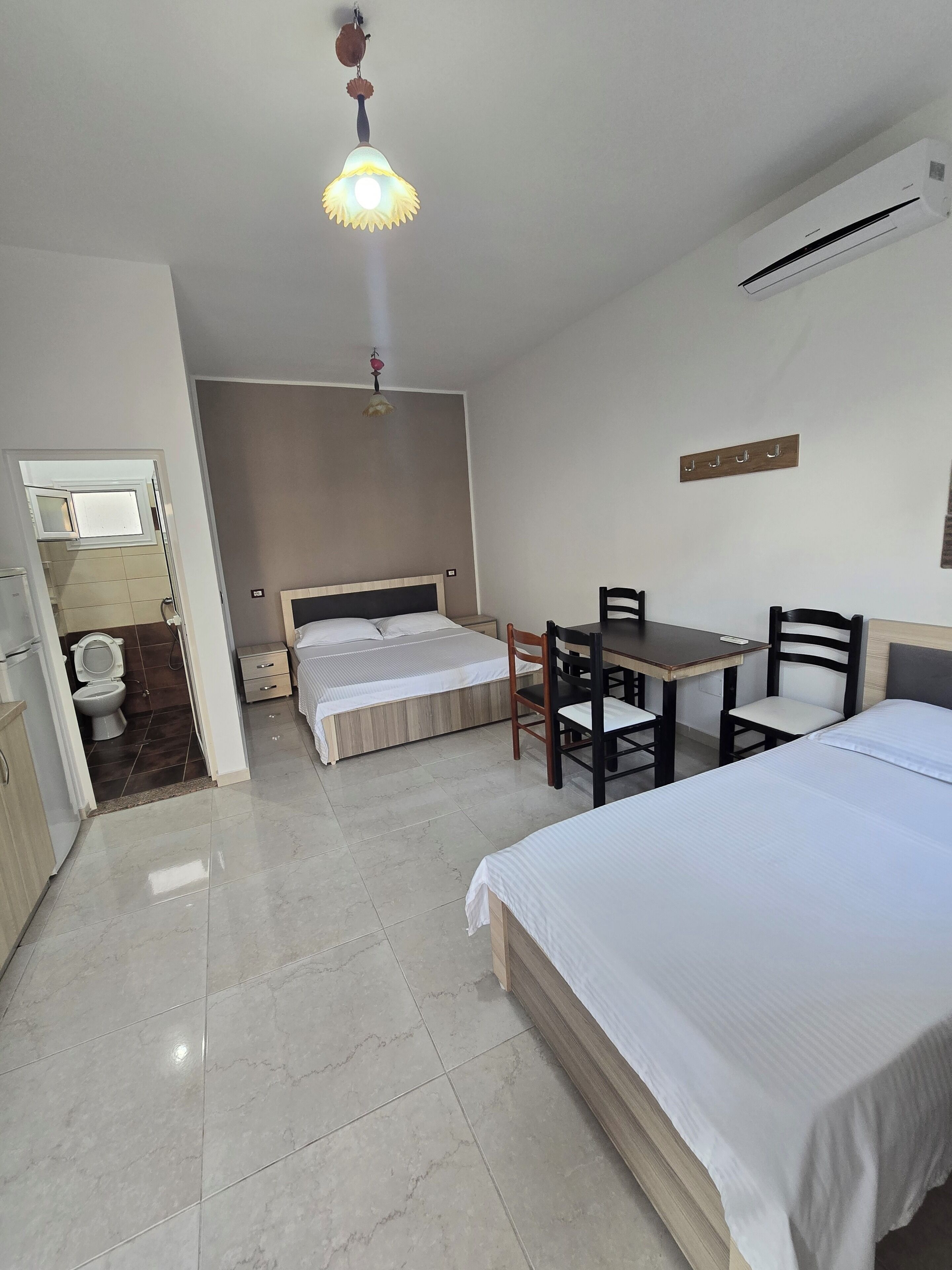 Une chambre d’hôtel comprenant un lit, un bureau avec des chaises, une petite table, un ventilateur de plafond et un climatiseur fixé au mur.