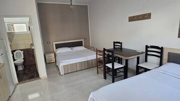 Une chambre d’hôtel comprenant un lit, un bureau avec des chaises, une petite table, un ventilateur de plafond et un climatiseur fixé au mur.
