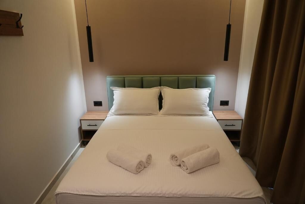 Habitación de hotel con una cama, dos mesitas de noche, un cabecero tapizado color verde y una lámpara colgante.