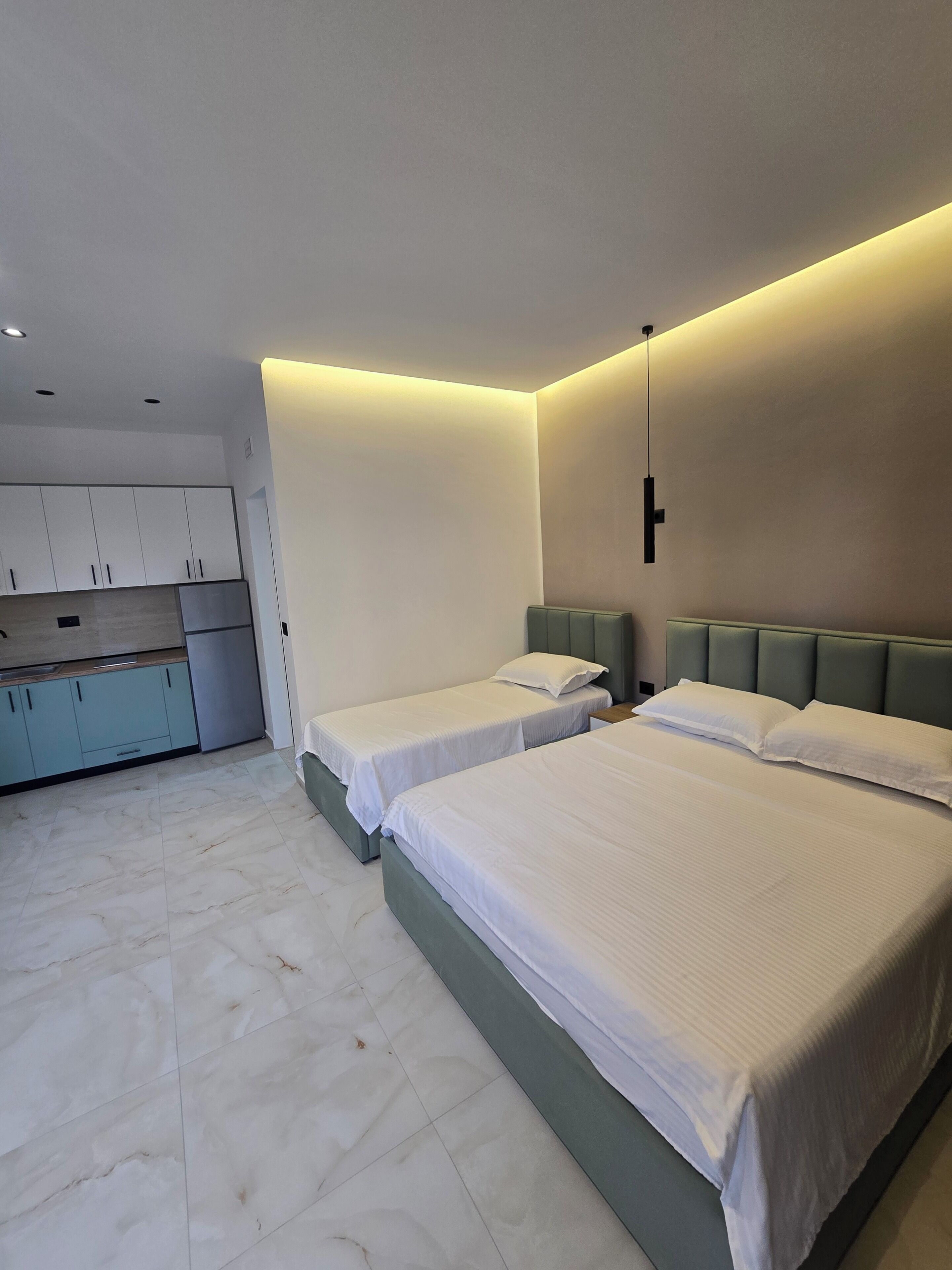 Un dormitorio moderno con dos camas, una kitchenette pequeña y una lámpara en el techo.
