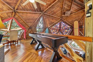 Ein Holzinterieur mit Billardtisch, Sitzecke und großen Fenstern.